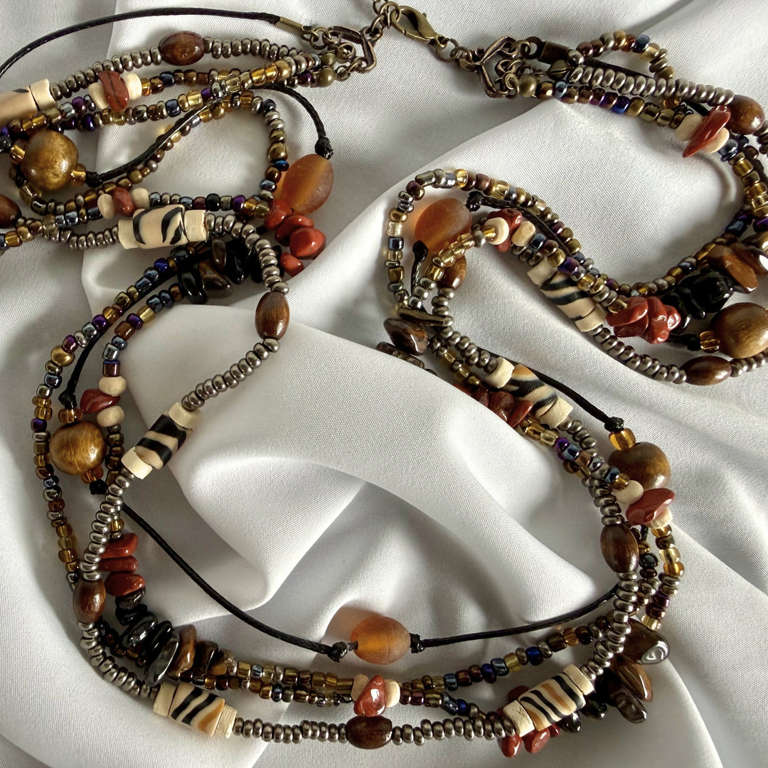 Top view of a handcrafted multi-strand necklace featuring layered chip beads, polymer clay, African print beads, and seed beads in warm earthy tones.