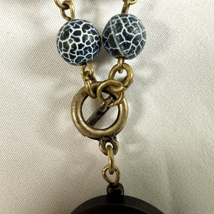 Close-up of antique brass clasp and cord fastening on a handcrafted pendant necklace.