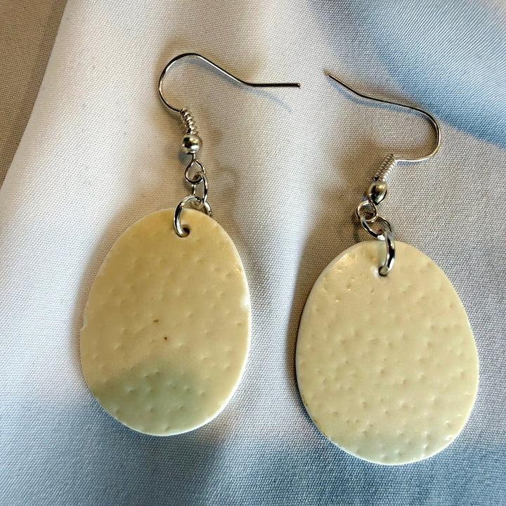 Two handcrafted oval ostrich eggshell drop earrings shown side by side with natural ivory tones and silver-tone hardware.