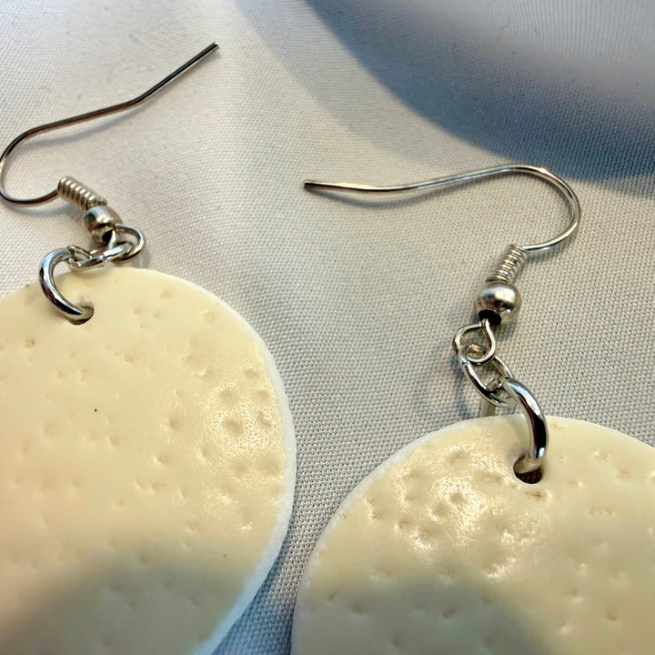 Close-up of round ostrich eggshell drop earrings highlighting silver-tone hooks and metal components with natural ivory beads.