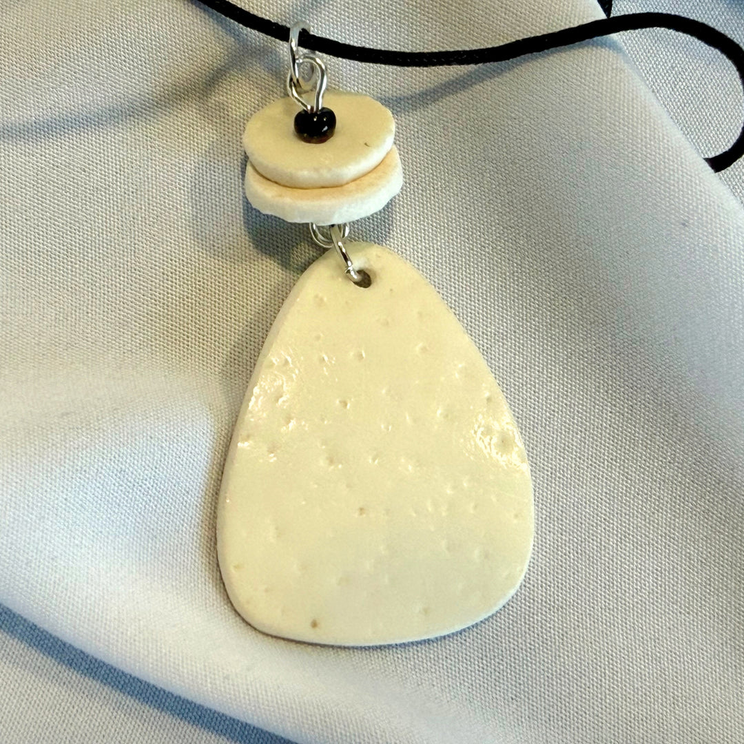 Angled close-up of an oval ostrich eggshell pendant showing natural texture and ivory colour variation.