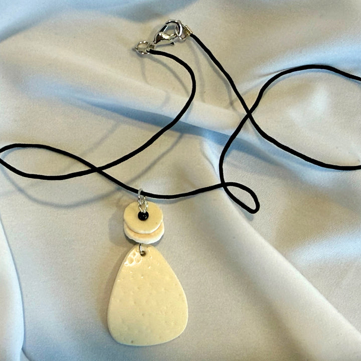 Full view of a handcrafted necklace featuring an oval ostrich eggshell pendant on black nylon cord.