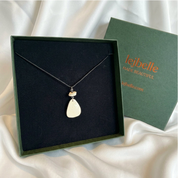Handcrafted ostrich eggshell pendant necklace displayed in a gift box with black cord and brass details.