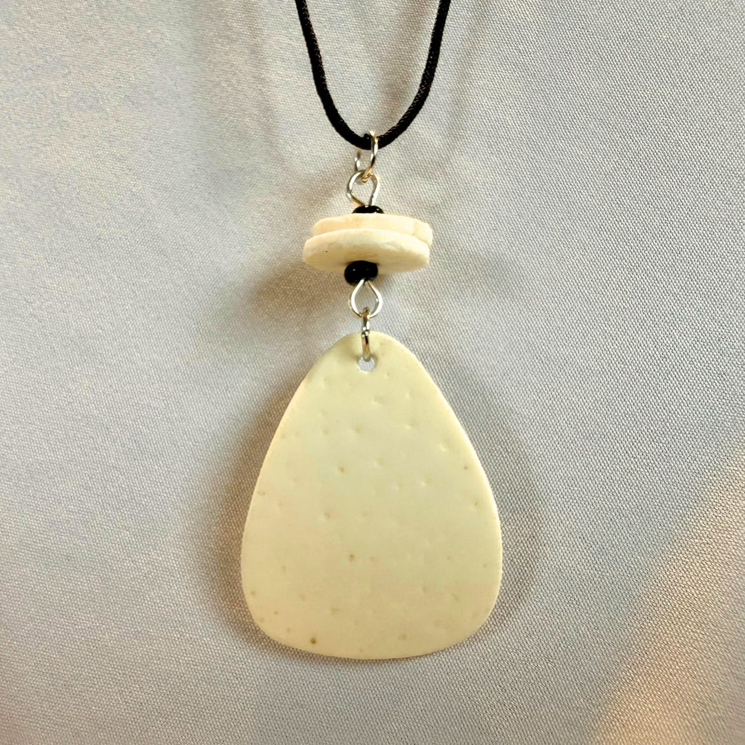 Top view close-up of a handcrafted ostrich eggshell pendant on black cord with brass fittings.