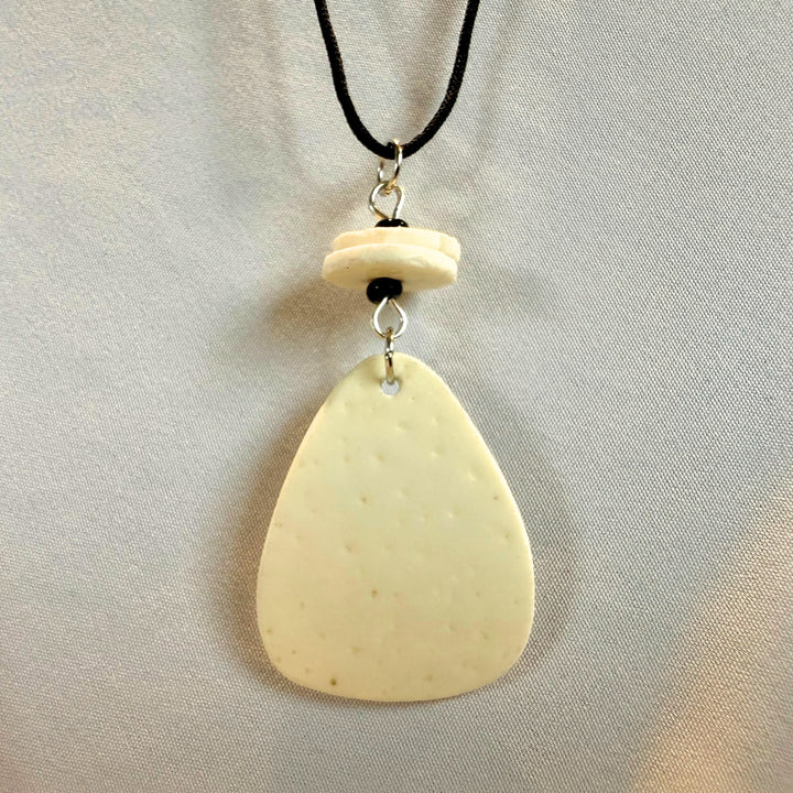 Top view close-up of a handcrafted ostrich eggshell pendant on black cord with brass fittings.