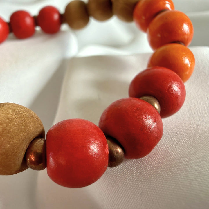 Close-up of a handcrafted bracelet showing red and orange wood beads with golden seed bead details.