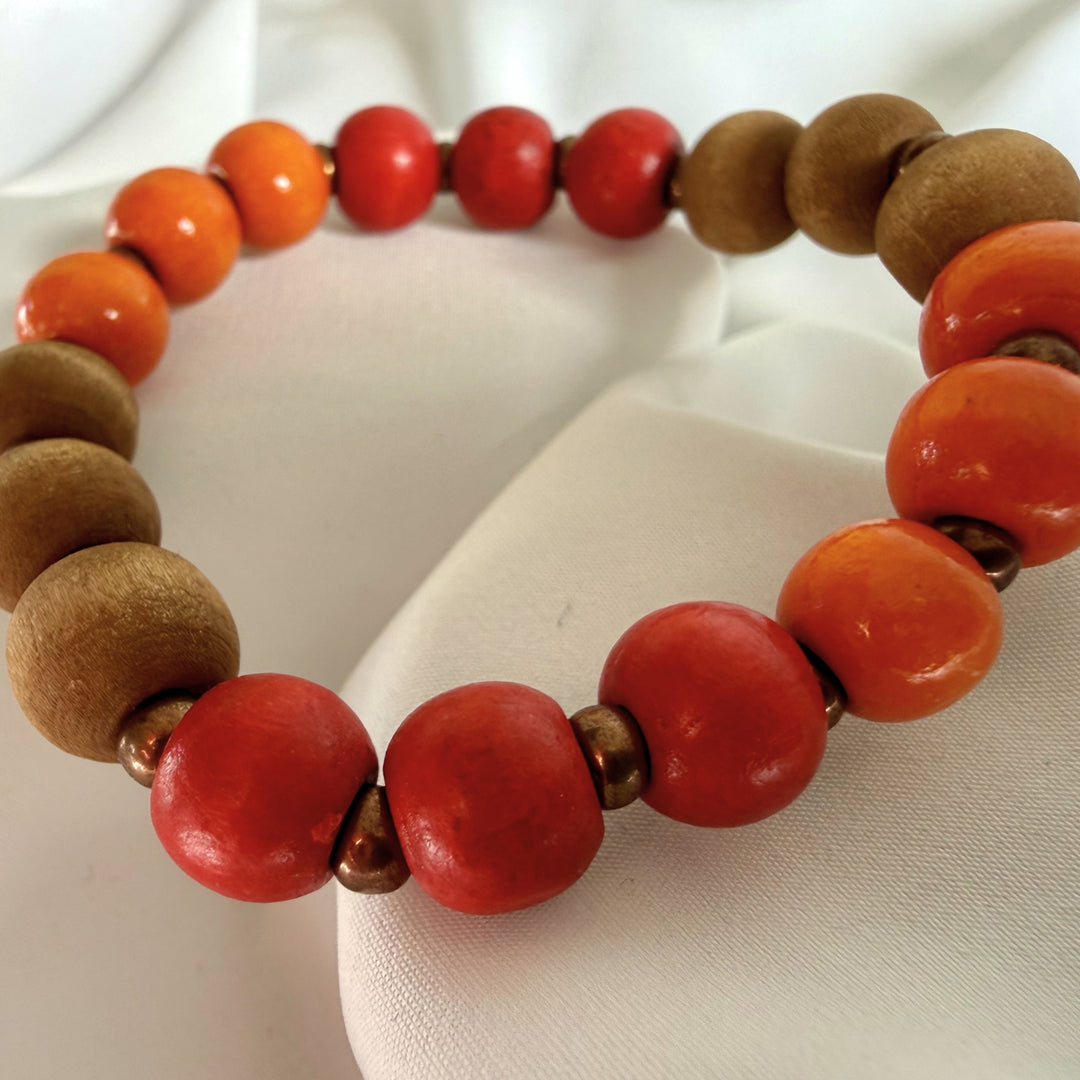 Full view of a handcrafted bracelet made with red, orange, and bronze-toned wood beads and golden seed bead accents.