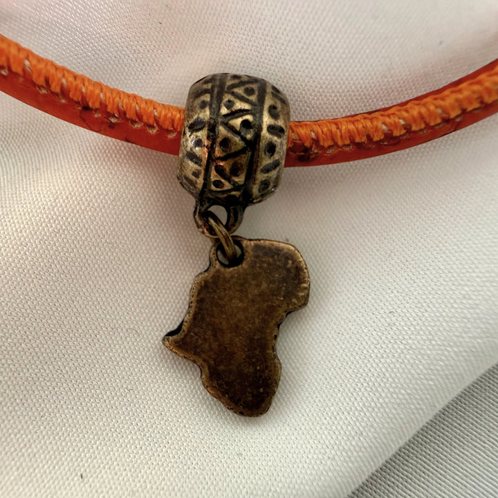 Close-up of Africa charm on a red cork bracelet with antique brass detailing.