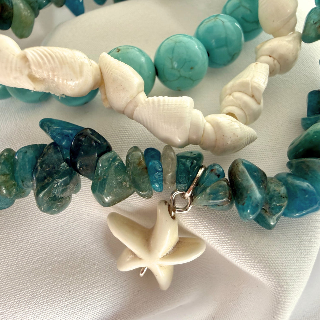 Close-up of layered turquoise and white bracelets with a white seastar charm in focus.