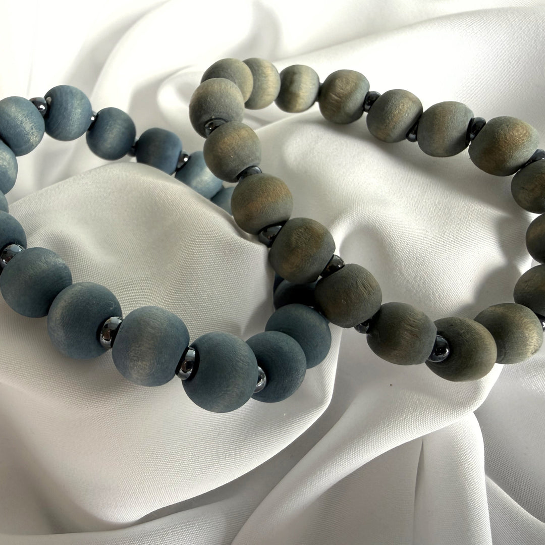 Full view of two handcrafted beaded bracelets in cool blue and grey tones made with wood and silver-coloured seed beads.