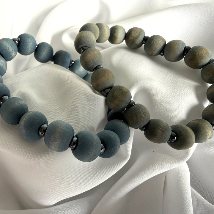 Full view of two handcrafted beaded bracelets in cool blue and grey tones made with wood and silver-coloured seed beads.