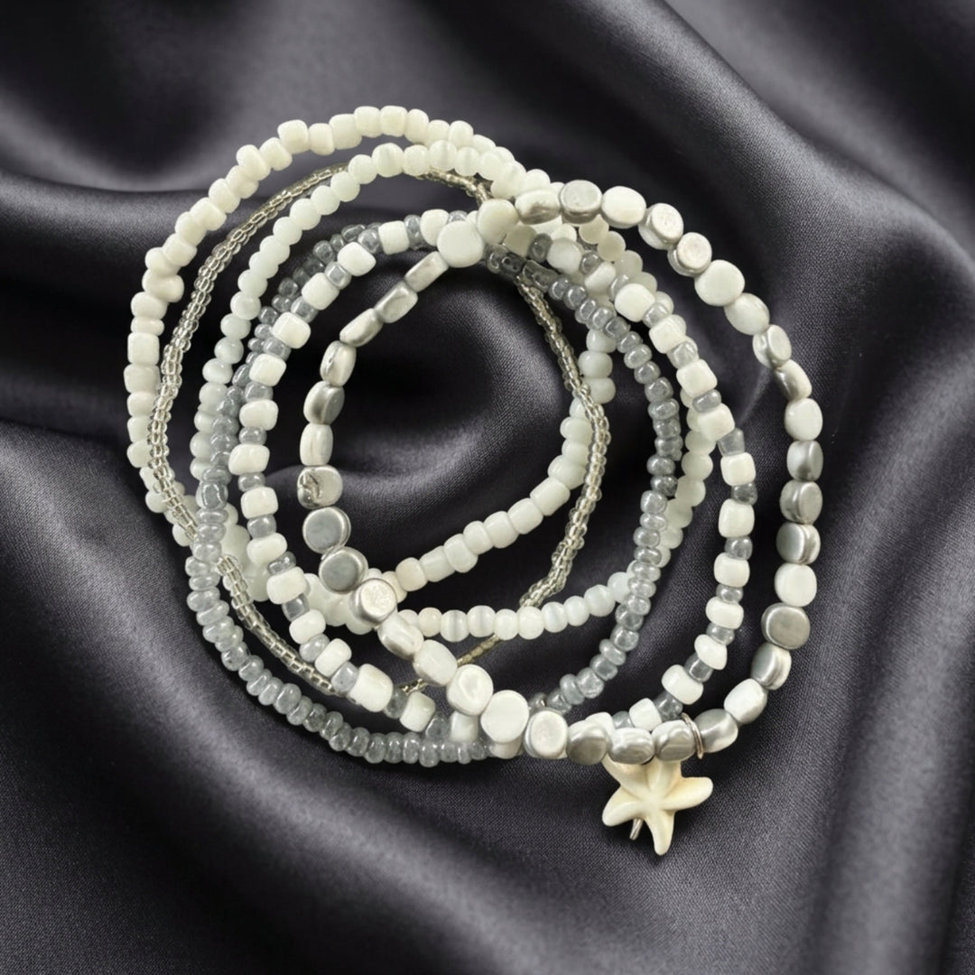 Full view of six handcrafted stackable bracelets with silver-tone and white beads displayed on dark grey silk fabric.