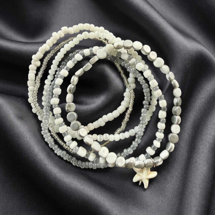 Full view of six handcrafted stackable bracelets with silver-tone and white beads displayed on dark grey silk fabric.