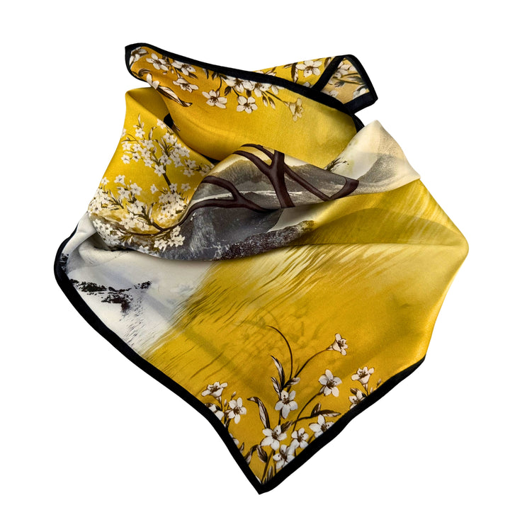 Partially folded silk scarf highlighting the smooth silk texture, black border, and multicolor landscape design.