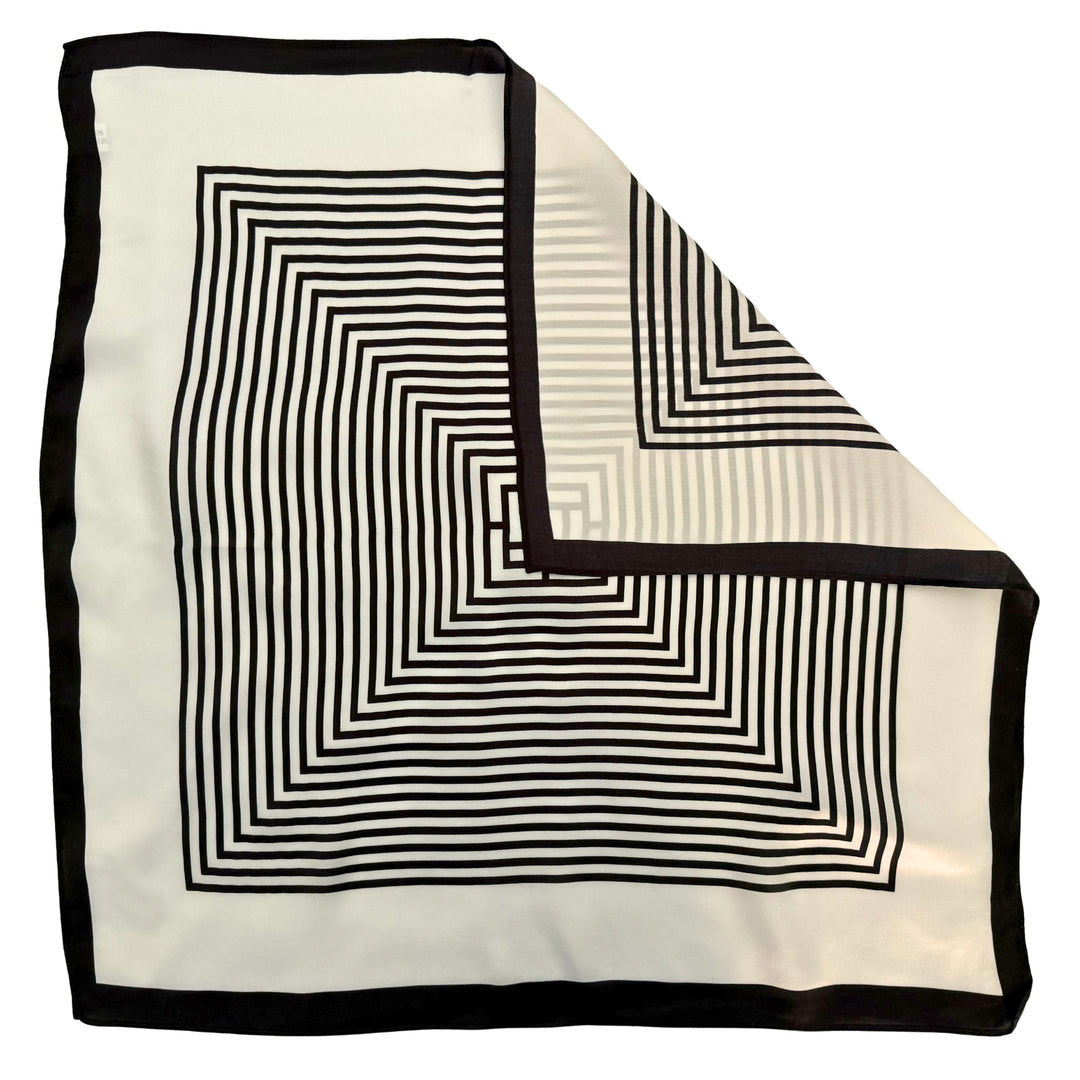 Top view of a silk scarf with one corner folded to show the reverse side of the tone-on-tone black and ivory labyrinth print.