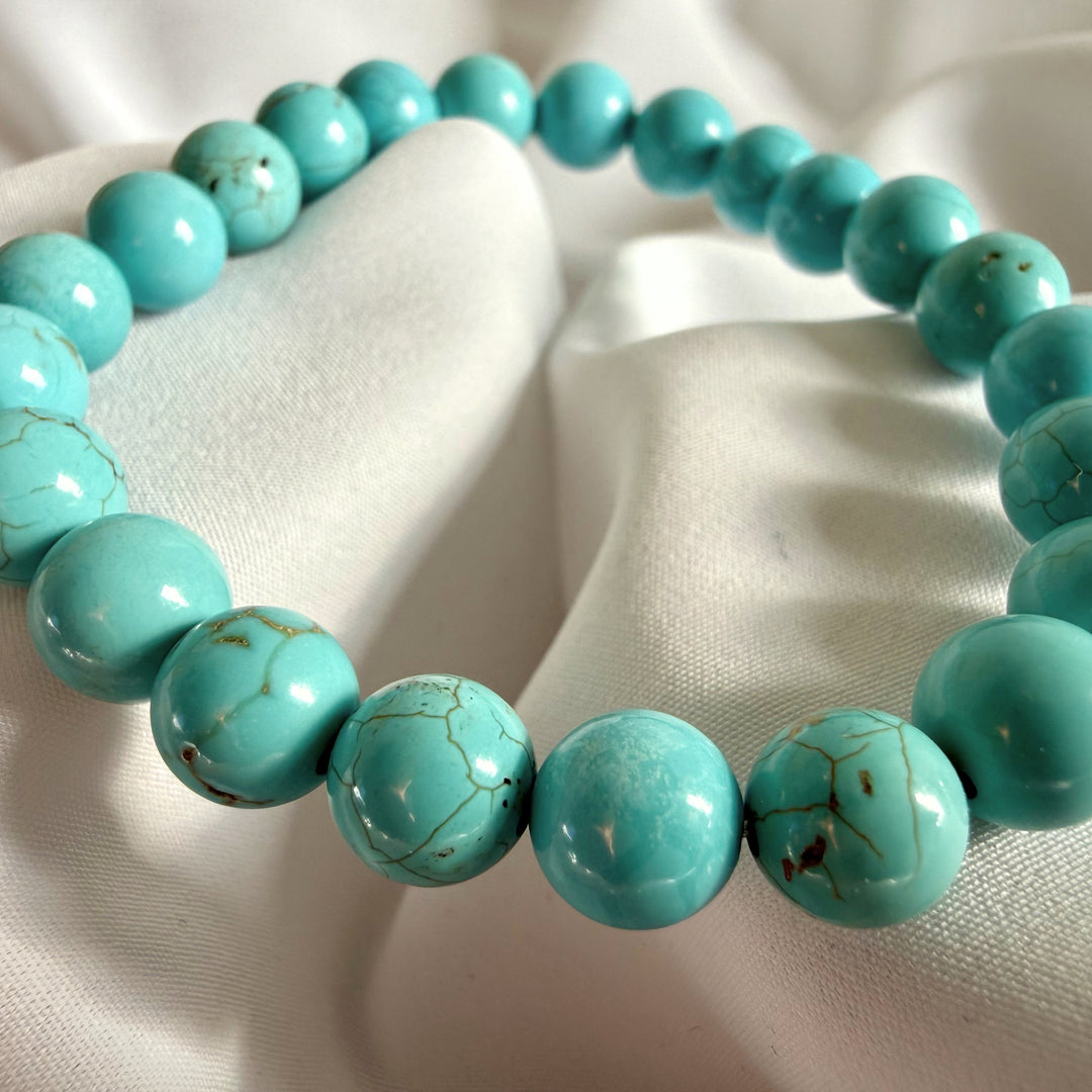 Angled full view of a handcrafted turquoise howlite bead bracelet on elastic cord.