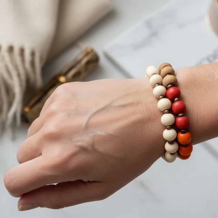 Set of two handcrafted beaded bracelets with wood and golden seed beads worn on a wrist, featuring red, orange, bronze, gold, and ivory tones.
