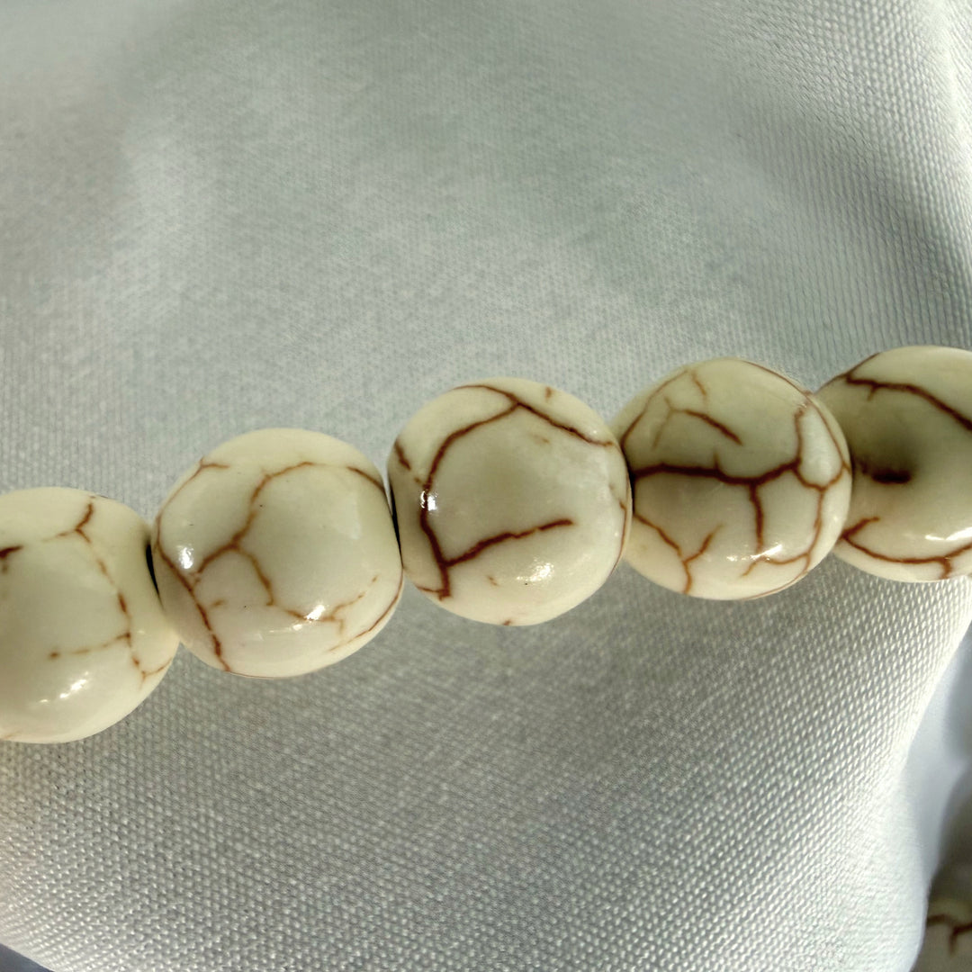 Close-up of smooth white howlite beads with natural brown veining on a handmade bracelet.