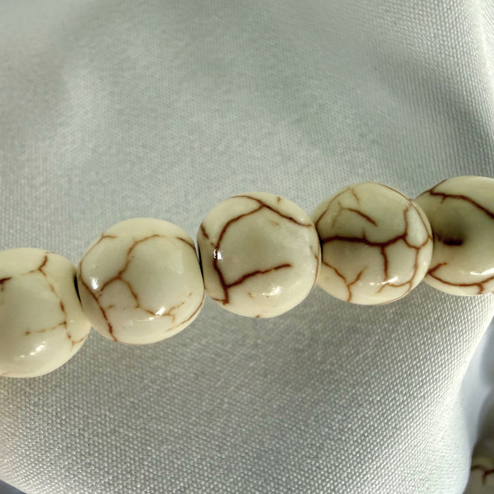 Close-up of smooth white howlite beads with natural brown veining on a handmade bracelet.
