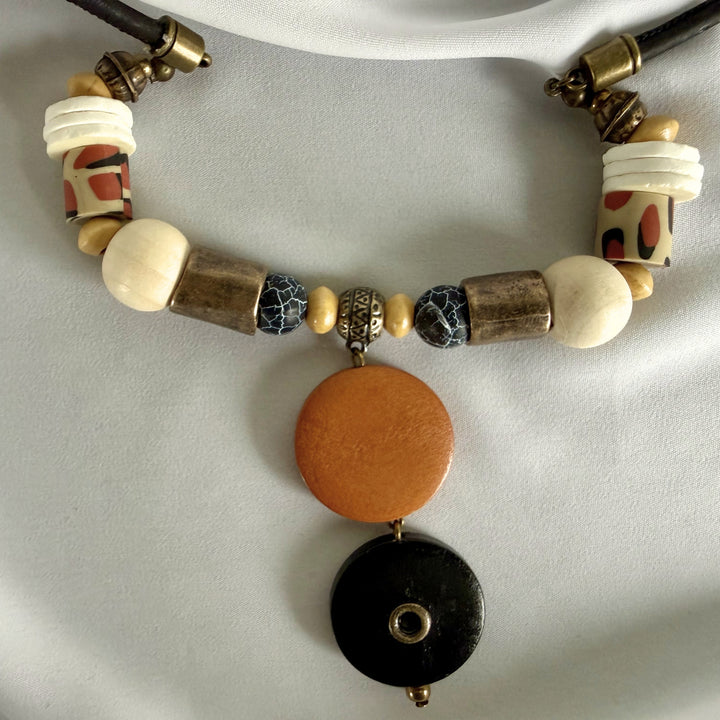 Close-up of the lower pendant section of a handcrafted necklace showing wood, crackle agate, and mixed natural materials.
