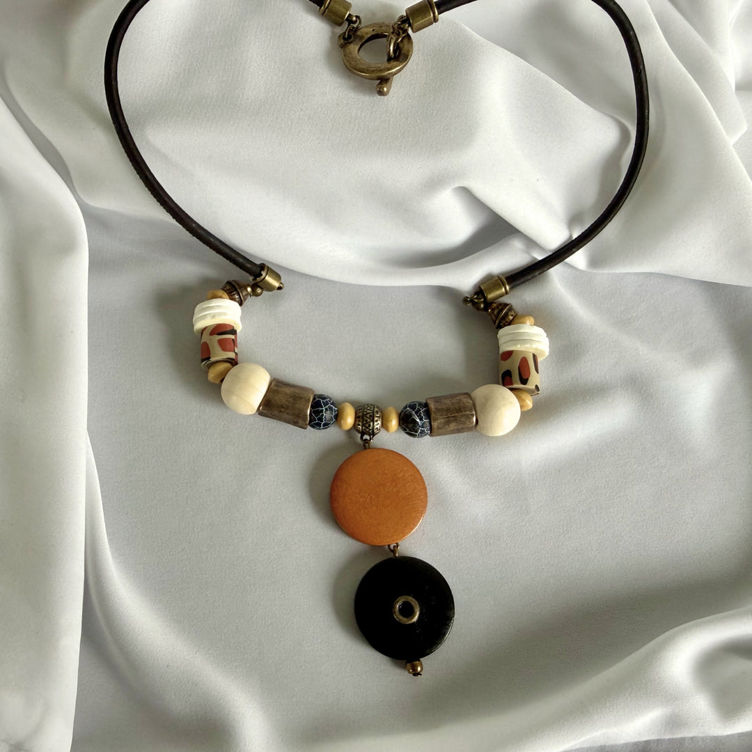 Full view of a handcrafted pendant necklace featuring wood, crackle agate, polymer clay, and ostrich eggshell accents on black cork cord.