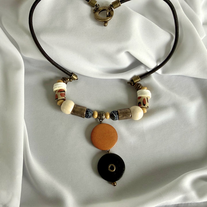 Full view of a handcrafted pendant necklace featuring wood, crackle agate, polymer clay, and ostrich eggshell accents on black cork cord.