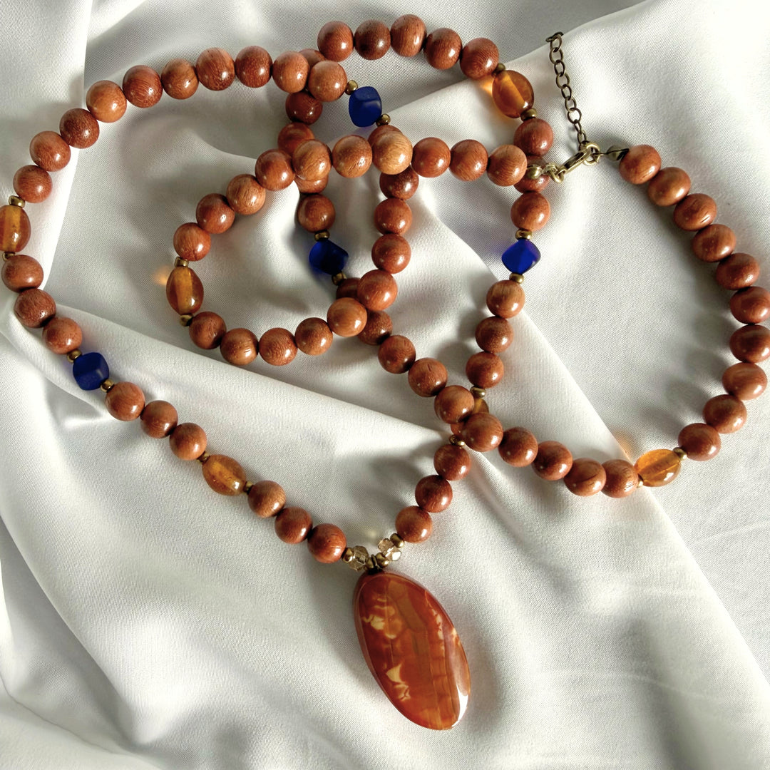 Top view of a handcrafted necklace featuring wooden beads, oval amber beads, and blue glass accent beads.