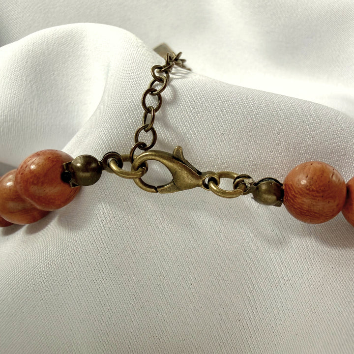 Close-up of adjustable clasp and antique brass chain extension on a handcrafted wooden and amber beaded necklace.