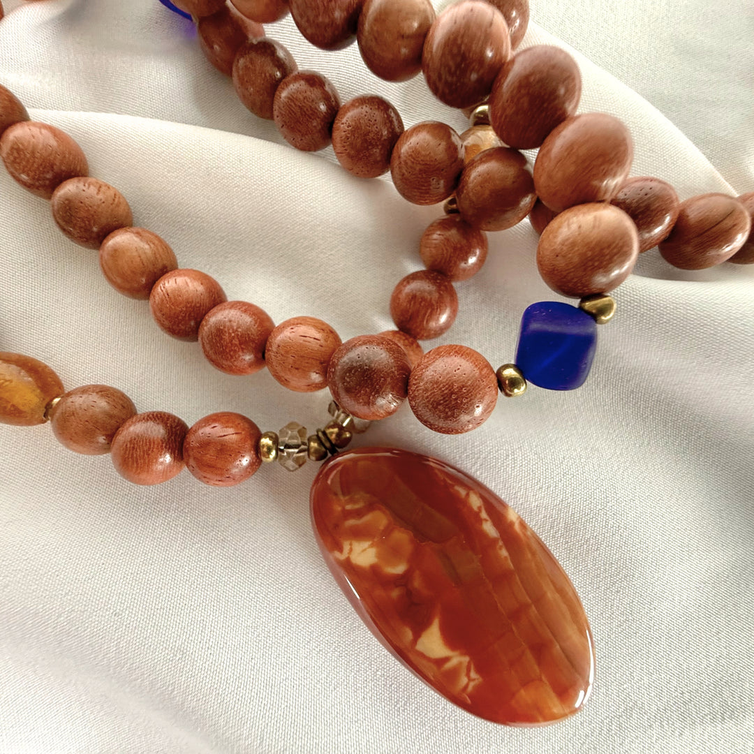 Side close-up of a handcrafted necklace showing wooden beads and amber beads with mixed textures and colour contrast.