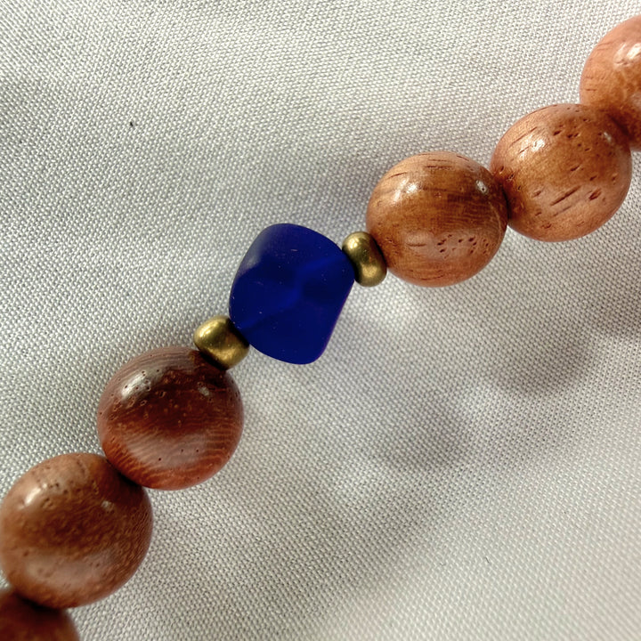 Close-up of wooden beads paired with a blue square glass bead on a handcrafted necklace.