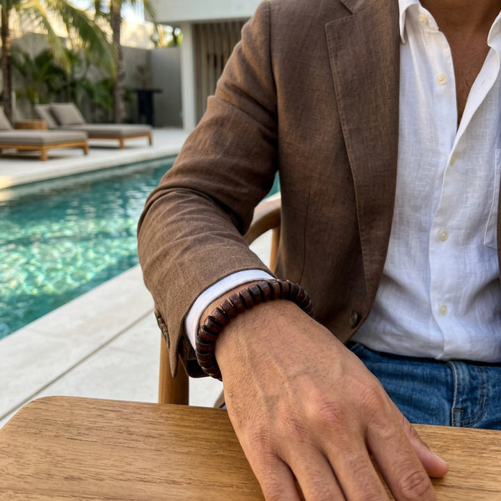 A man by a pool showing only his wrist wearing a brown flat wooden beaded bracelet.